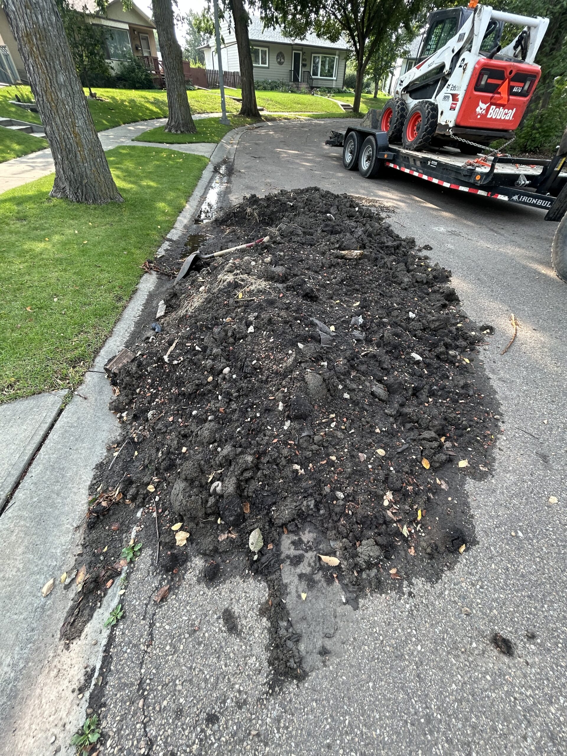 Skidsteer/Bobcat Services Edmonton - Skidsteer on a trailer next to topsoil